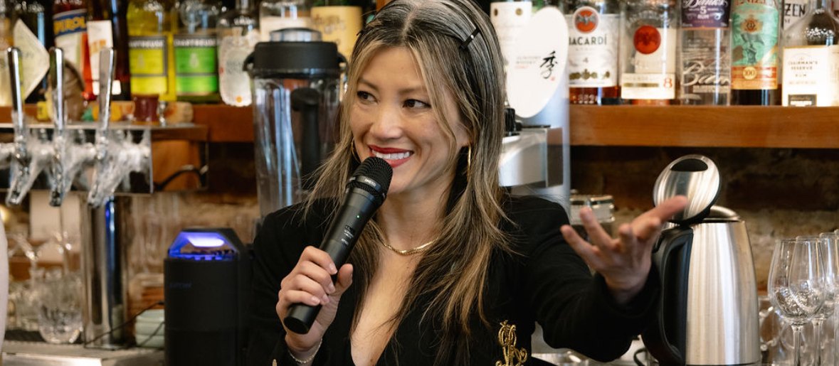 Jaymee Mandeville speaking with a microphone behind a back bar