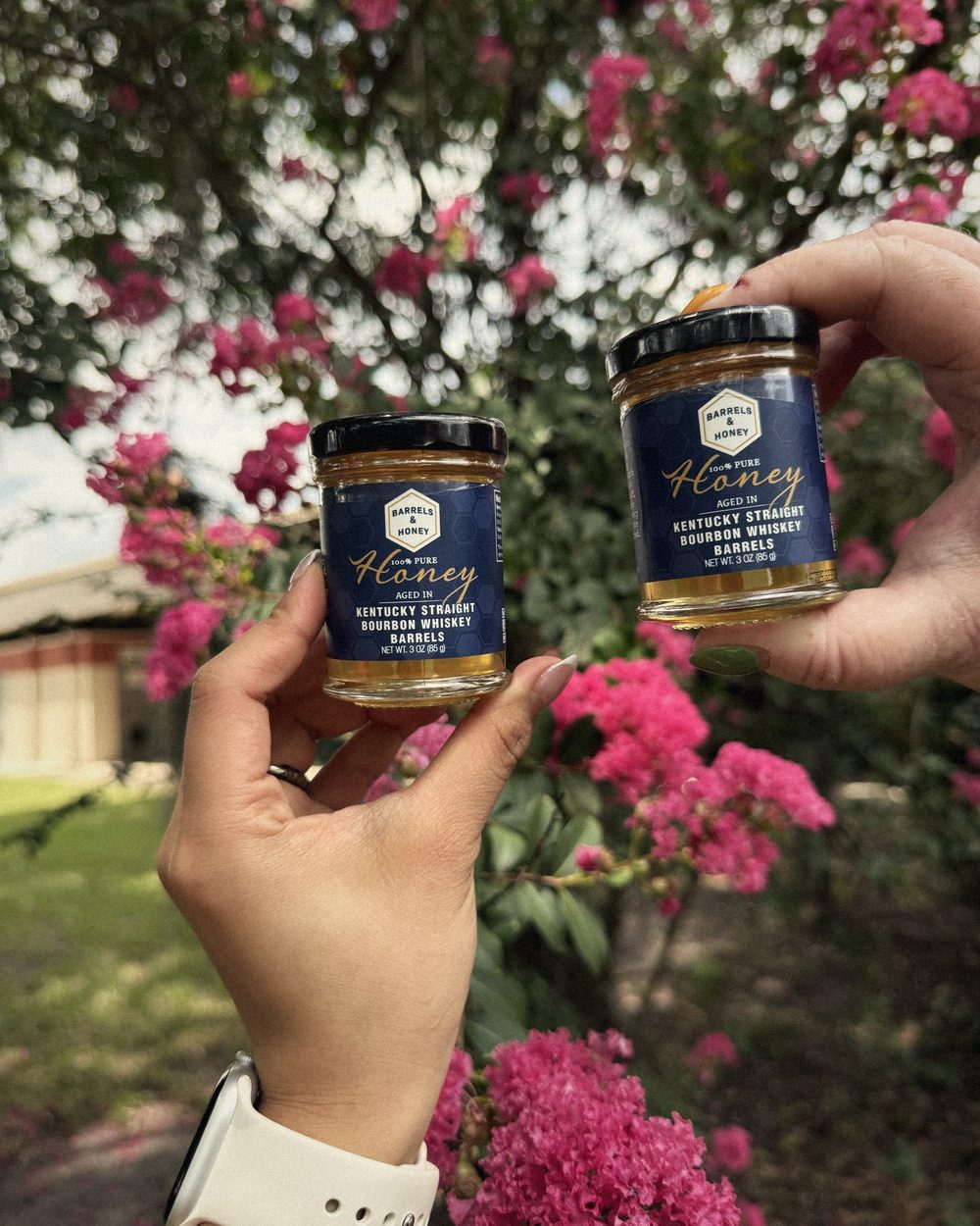 Two jars of Barrels & Honey held up among flowers